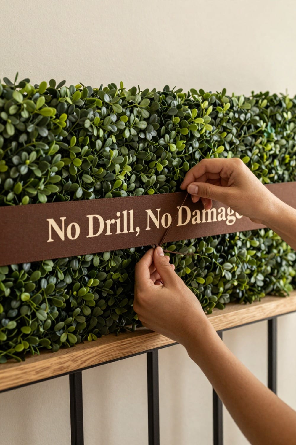 Hands threading a color-matched zip tie through a faux hedge panel backing and around a balcony railing bar